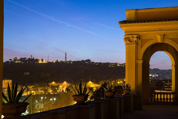 A balcony with potted plants and a view of a cityscape at dusk. - Best Western Hotel Astrid (Rome)