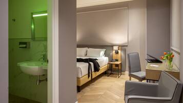 Ein Hotelzimmer mit Bett, Nachttisch, Lampe, Stuhl und einem Glastisch mit Blumenvase.
