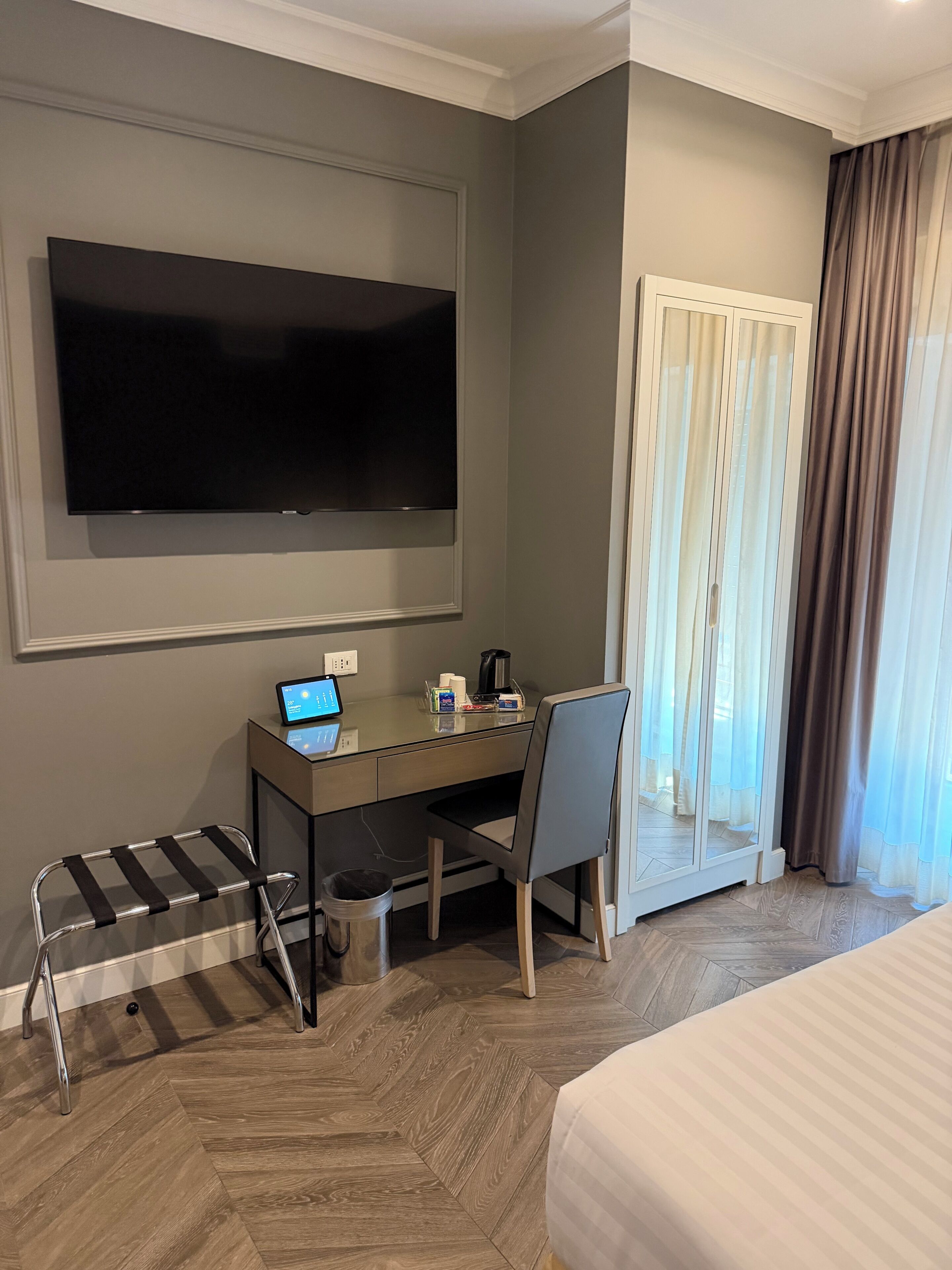 A hotel room with a bed, a desk with a laptop, a television, and a window with curtains.