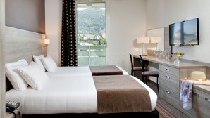 A hotel room with two beds, a desk with a TV, and a view of a mountain and buildings. - greet Lourdes Centre Pyrénées (Ouverture juin 2026) (Lourdes)