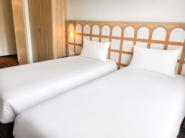 A double bed with a wooden headboard and two pillows, a wooden wardrobe, and a wall-mounted light fixture. - greet Lourdes Centre Pyrénées (Ouverture juin 2026) (Lourdes)