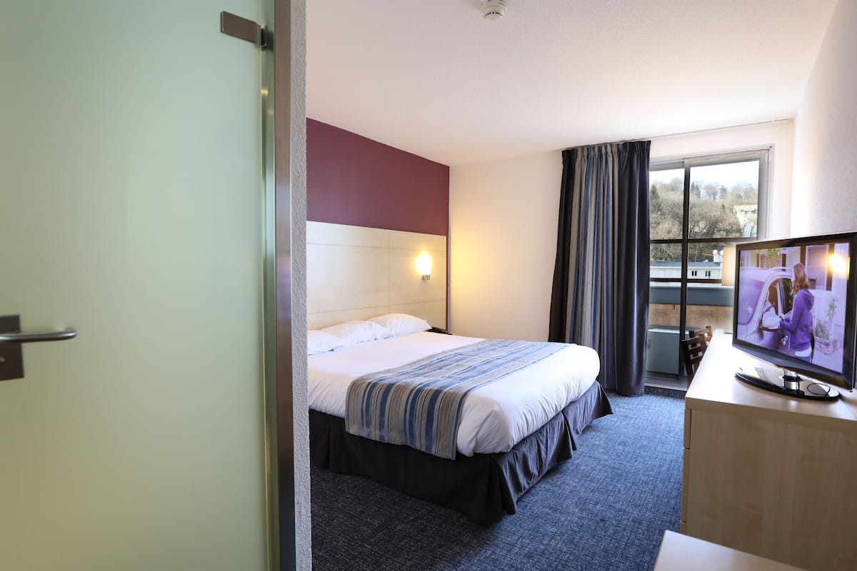 A hotel room with a bed, a television, a desk, and a window with curtains.