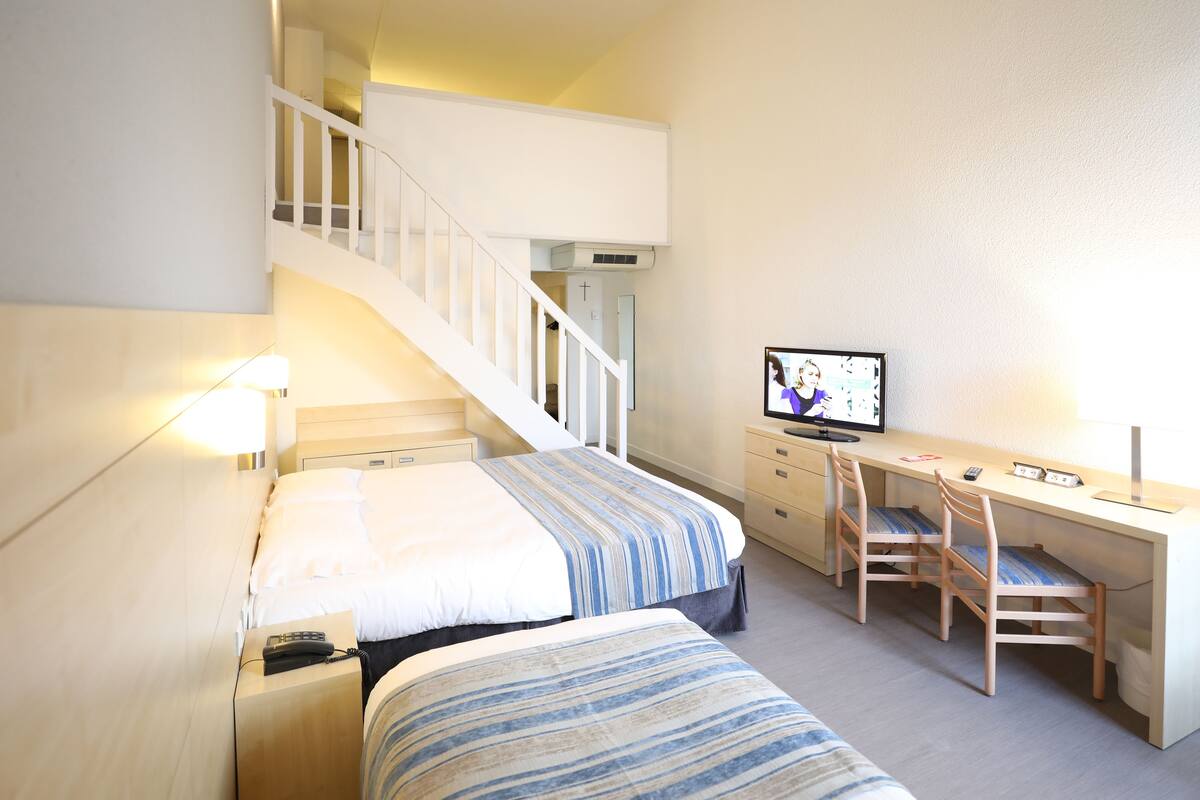 A hotel room with a bed, a desk, a chair, a television, and a staircase.