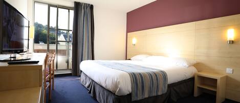 A hotel room with a bed, a desk with a chair, a TV, a window with curtains, and a nightstand.