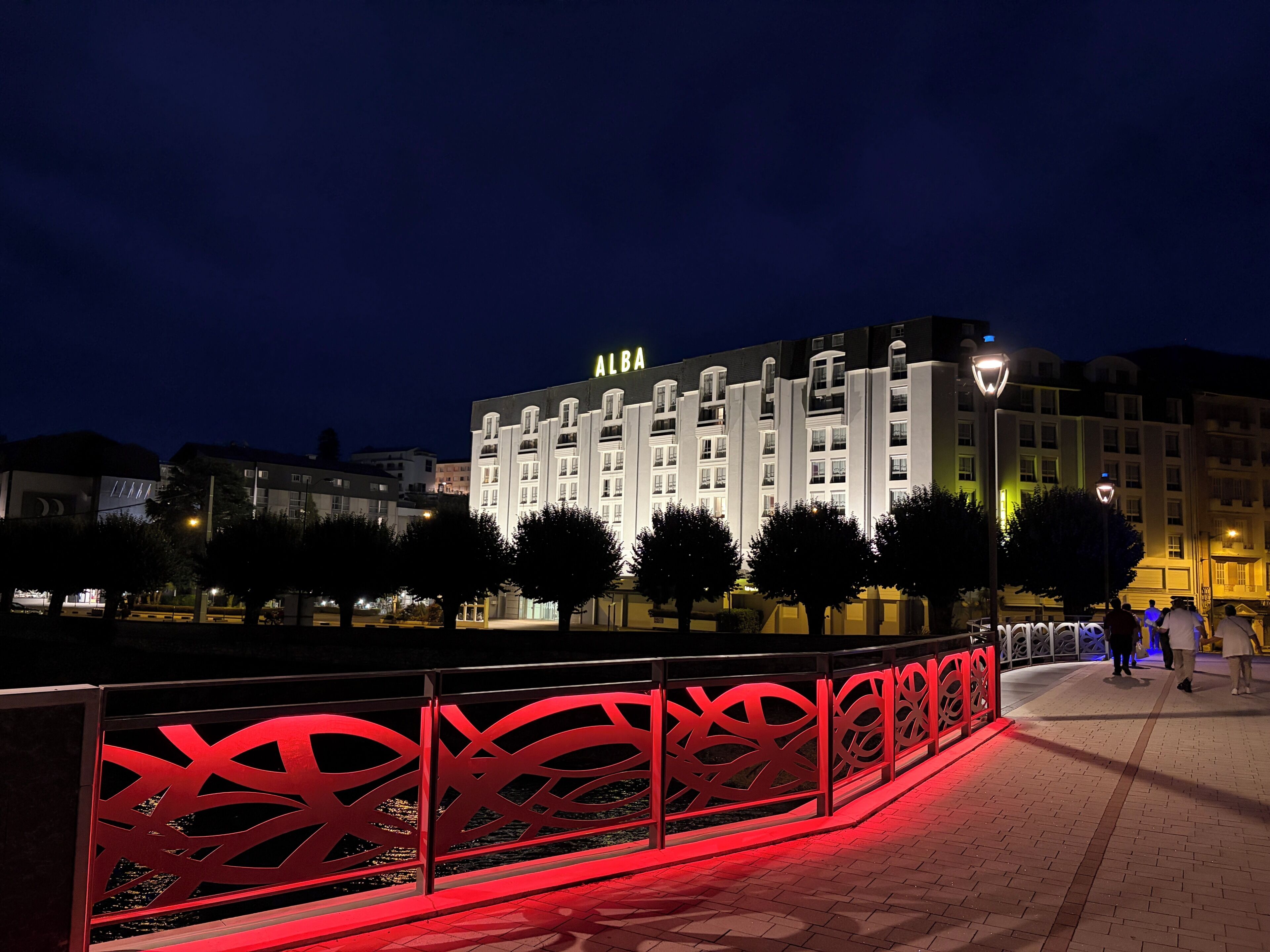 A hotel with a prominent 'ALBA' sign, a red decorative fence, and a paved walkway.