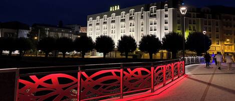 Un hôtel reconnaissable à son grand panneau « ALBA », à sa clôture décorative rouge et à son chemin piétonnier dallé.