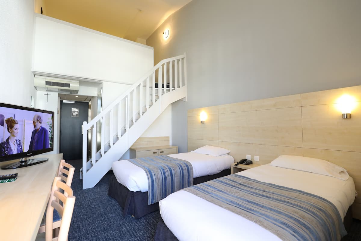 A hotel room with two beds, a TV, a desk with a chair, and a staircase.