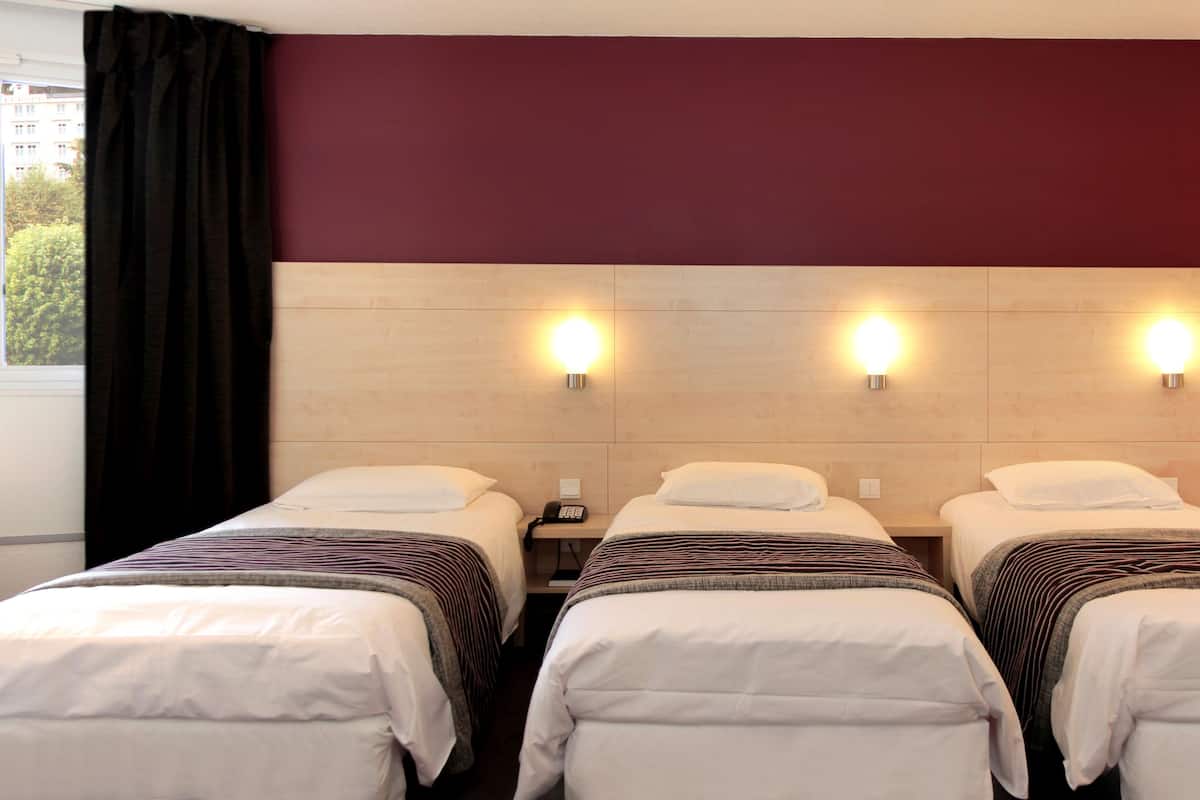 A hotel room with three single beds, a wooden headboard, and bedside lamps.