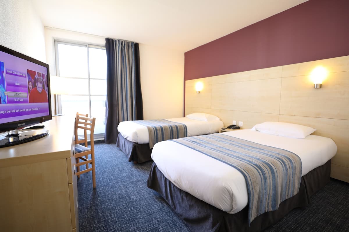 A hotel room with two beds, a desk with a television, and a chair.