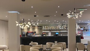 En moderne café med runde borde og stole, et barområde med et udvalg af drikkevarer, og et loft med indbygget belysning.