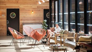 A modern interior with wooden panel walls, large windows, and a mix of seating including orange chairs and a sofa. - Camping de Paris (Paris)