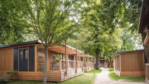 A row of wooden cabins with large windows and a covered porch area, surrounded by trees. - Camping de Paris (Paris)