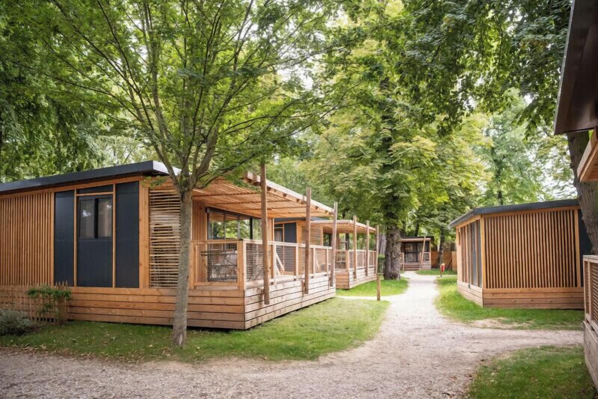 Une rangée de cabanes en bois dotées de grandes fenêtres et d’un porche couvert, le tout entouré d’arbres.
