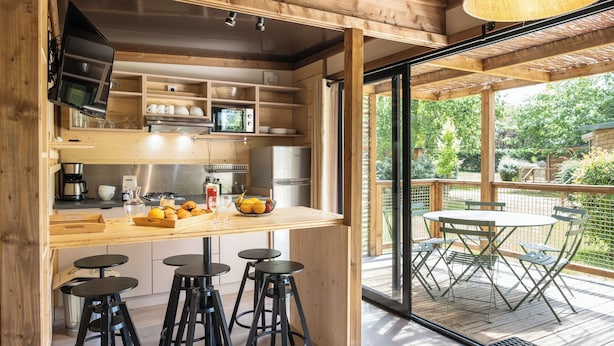 A wooden kitchen with a bar area, bar stools, and a view of the outdoor deck. - Camping de Paris (Paris)