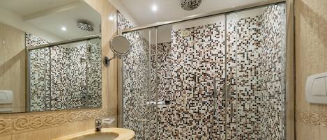 A modern bathroom with a glass-enclosed shower, a beige sink, and a tiled mosaic wall.