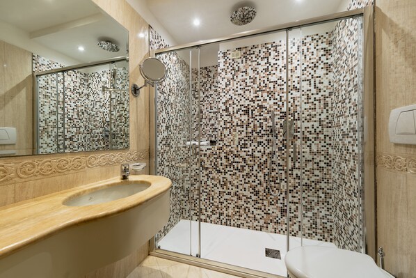 A modern bathroom with a glass-enclosed shower, a beige sink, and a tiled mosaic wall. - Hotel Antico Doge (Venice)