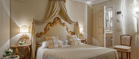 A classic four-poster bed with a canopy, a bedside table with a lamp, and a chair in a well-lit room with a wooden floor.