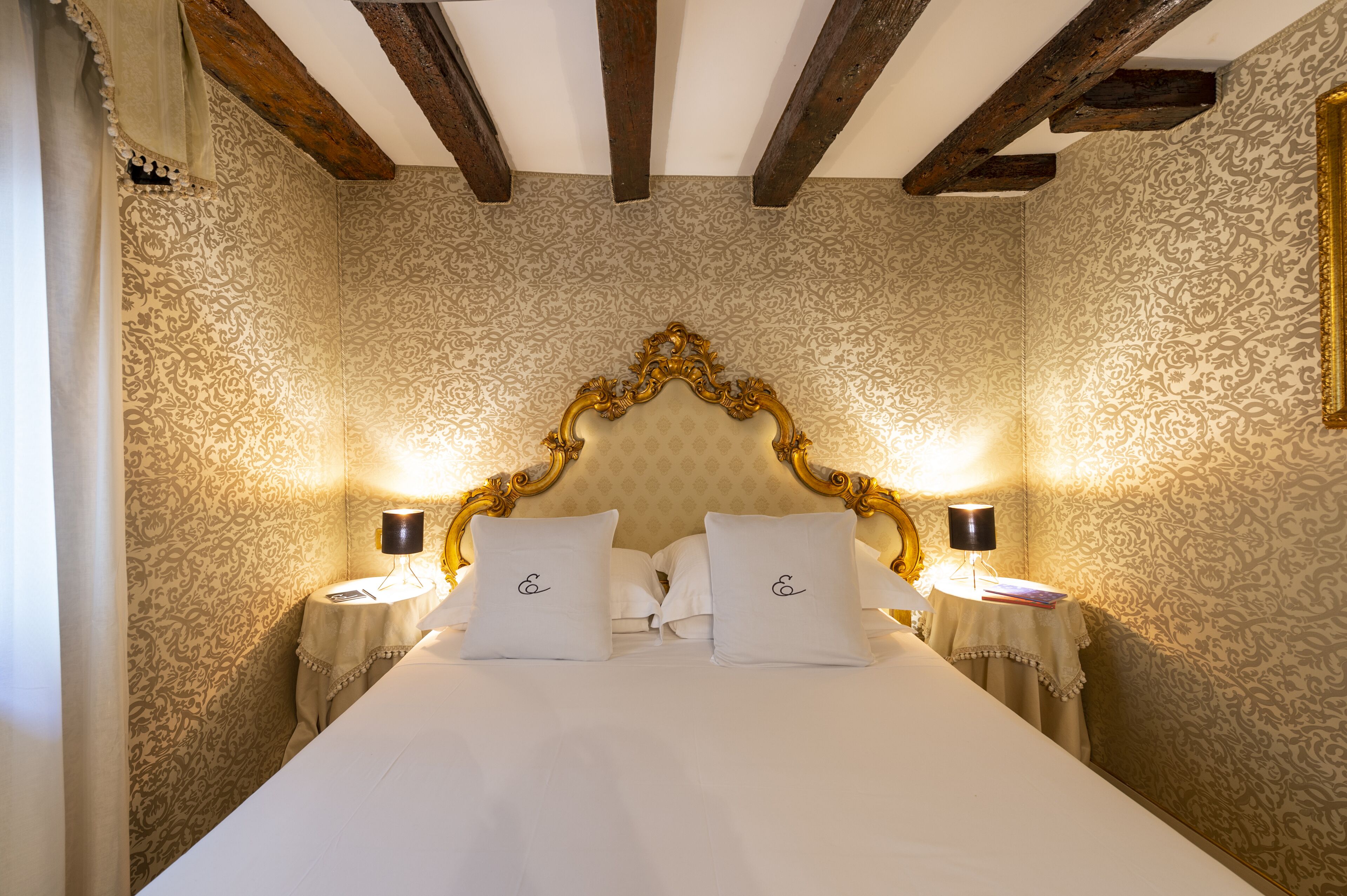 Een slaapkamer met een groot bed, een gedetailleerd hoofdeinde en twee bedlampjes.