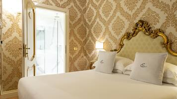 A hotel room with a large bed, ornate headboard, and patterned wallpaper.