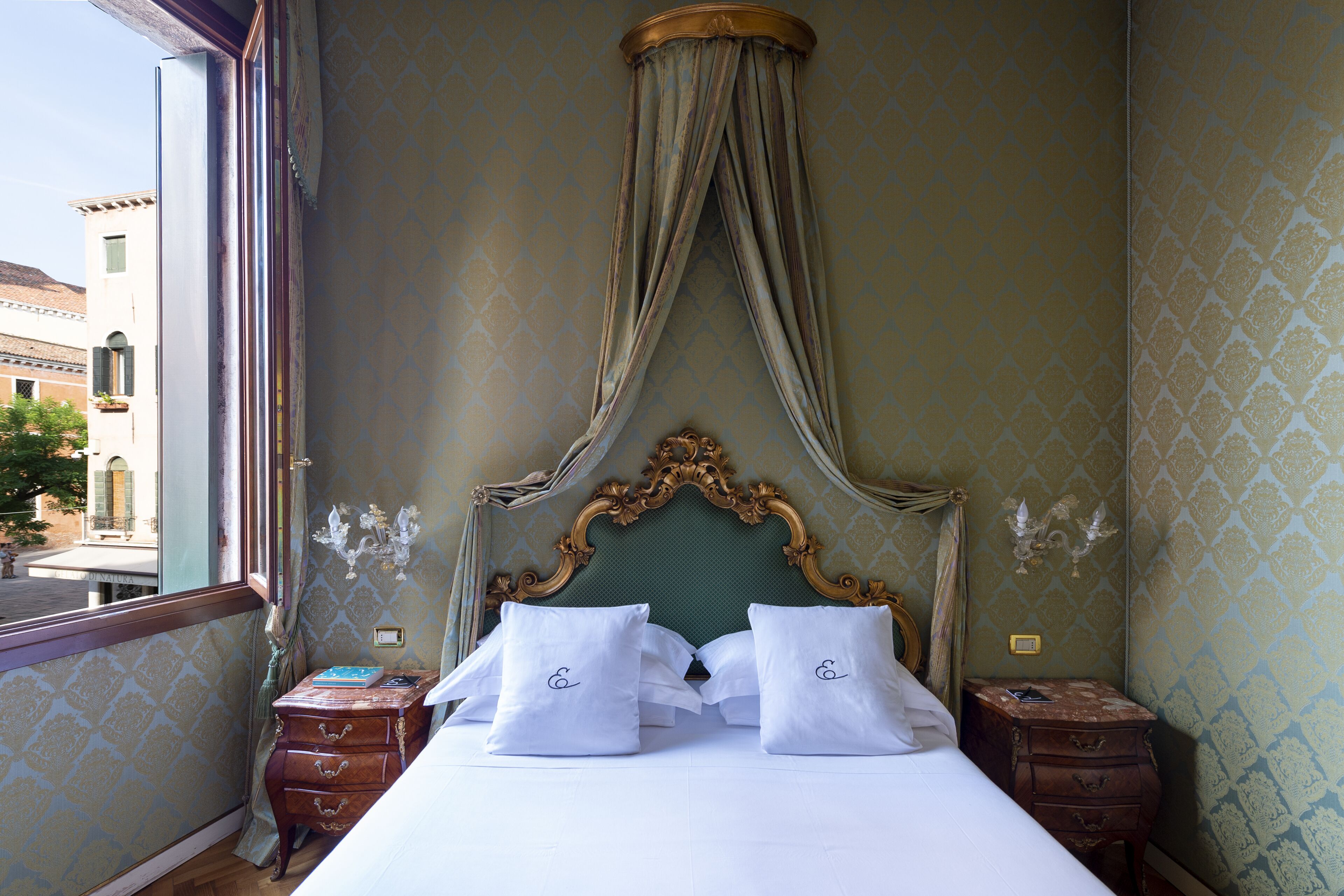 Une chambre dotée d’un grand lit, d’une tête de lit décorée et offrant une vue sur un bâtiment à l’extérieur.