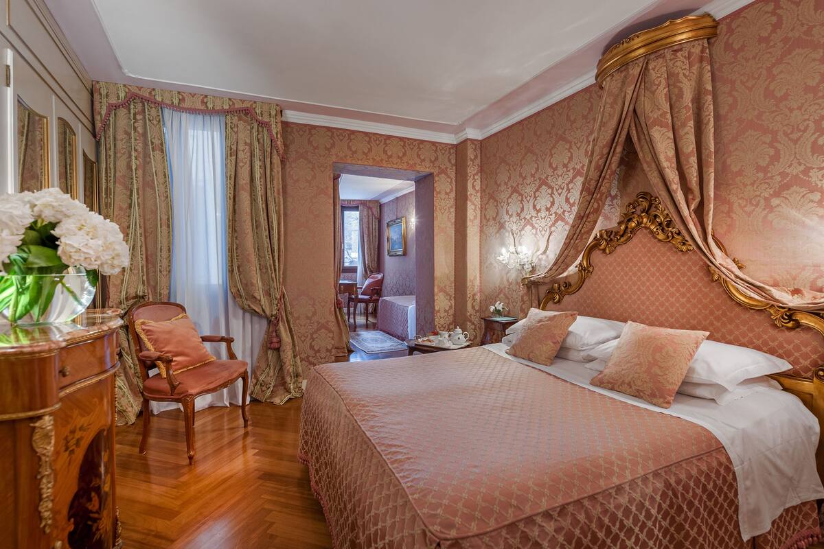 A bedroom with a large bed, a wooden chair, a side table, and a vase with flowers.