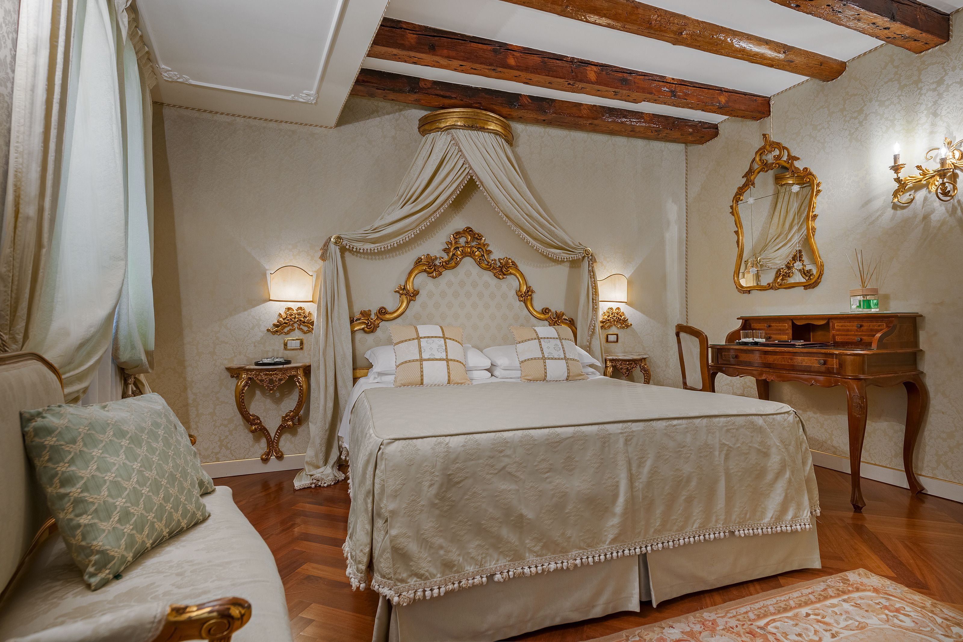 Un dormitorio con cama con dosel, un escritorio de madera, un espejo y una mesita de noche con lámparas.