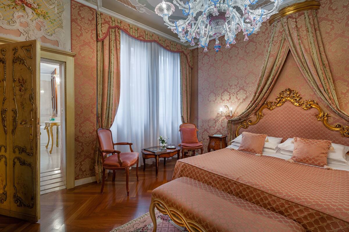 A bedroom with a large bed, a chandelier, and a view of the hallway.