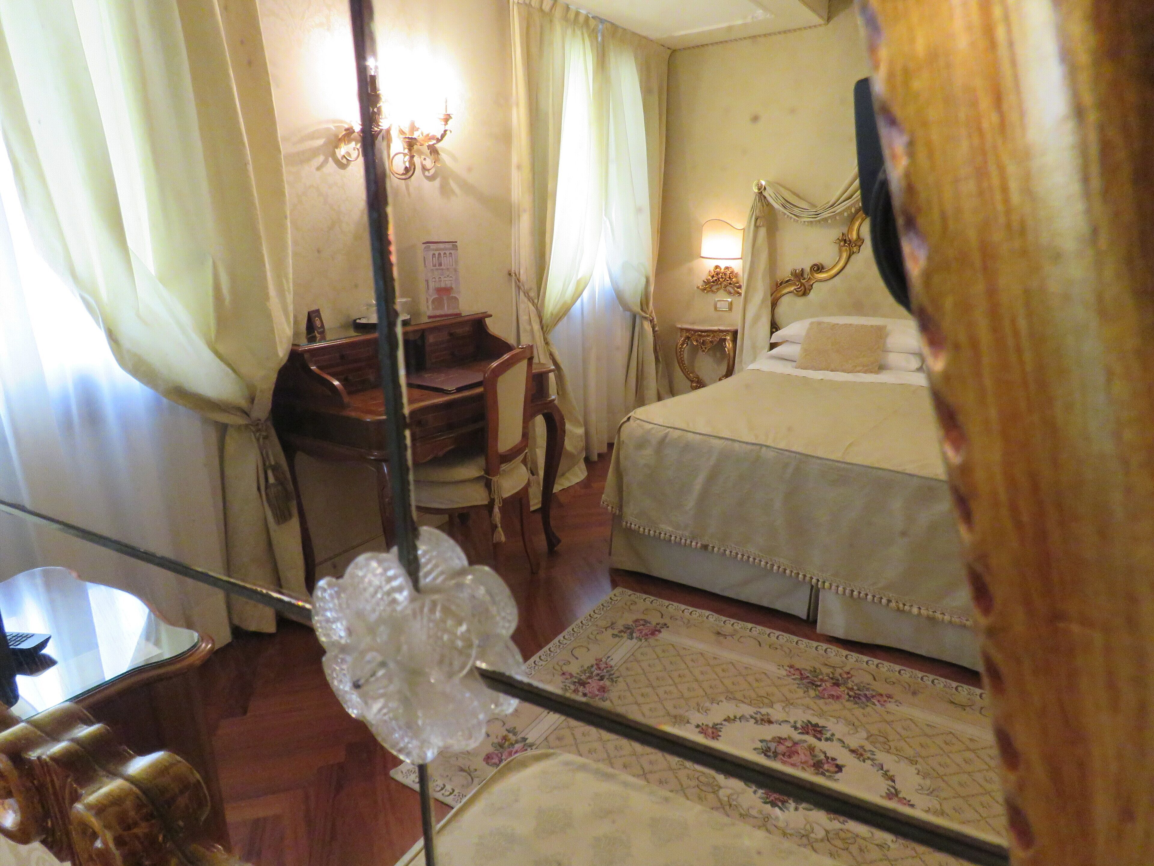 Habitación de hotel con una cama, un escritorio y una silla. Hay una lámpara en el escritorio y un espejo en la pared.