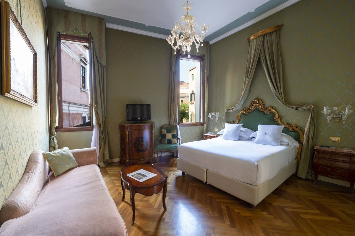 A hotel room with a large bed, a sofa, a small table, and a television.