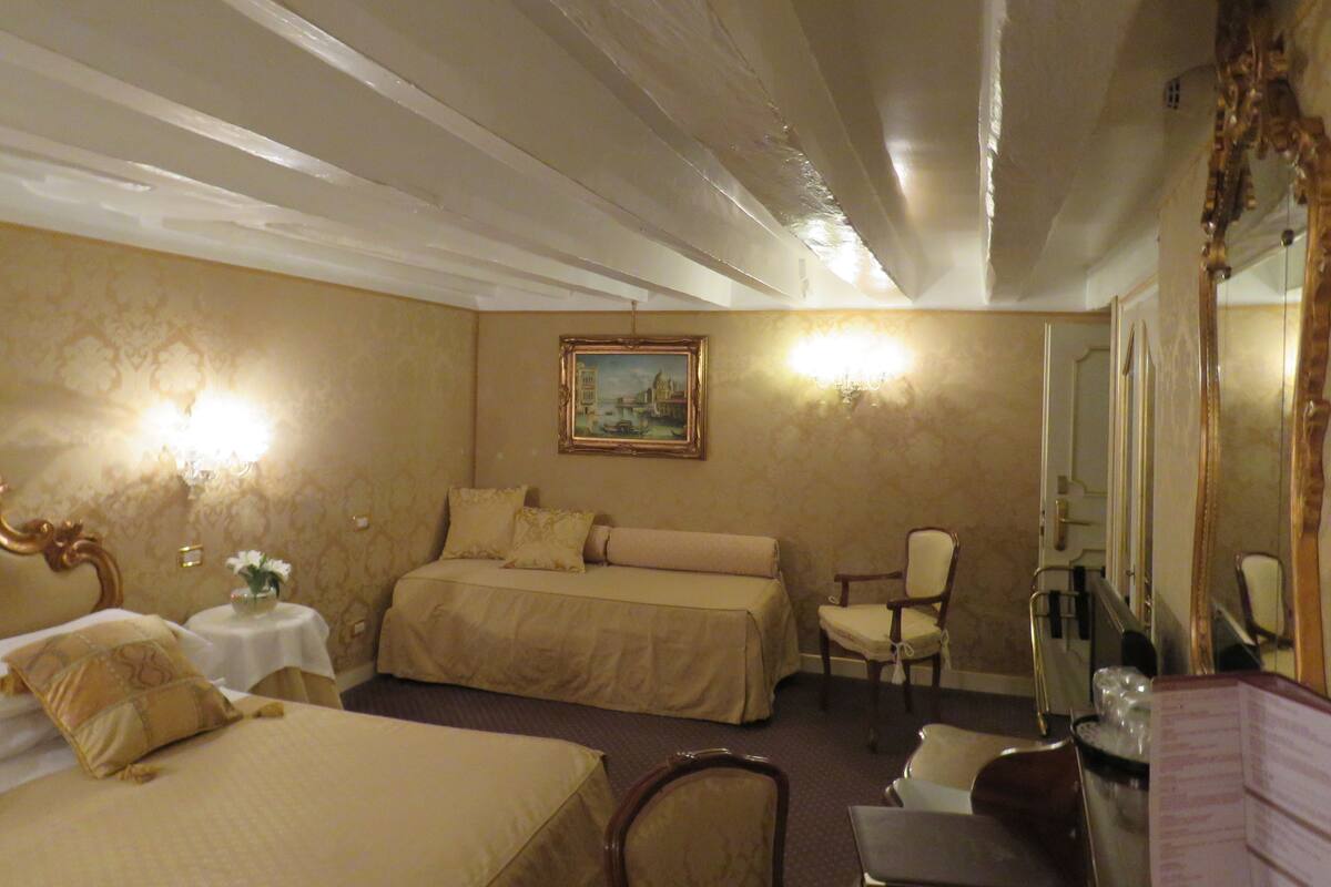 A hotel room with two beds, a chair, a table, a mirror, and a painting on the wall.