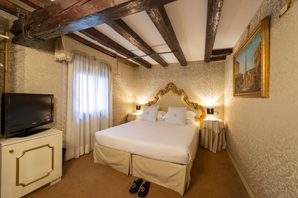 A hotel room with a large bed, a television on a cabinet, and a painting on the wall.