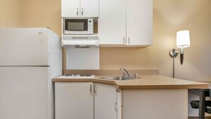 A compact kitchen with a refrigerator, microwave, sink, and a wall-mounted light fixture. - Extended Stay America Select Suites - Detroit - Roseville (Roseville)
