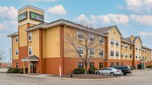 A multi-story hotel with a yellow facade, a sign for 'extended stay America' on the top left, and a parking lot with cars. - Extended Stay America Select Suites - Detroit - Roseville (Roseville)