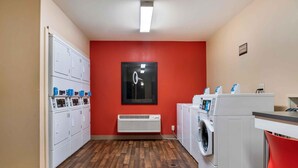 A laundry room with multiple washing machines, a dryer, and a wall-mounted mirror. - Extended Stay America Select Suites - Detroit - Roseville (Roseville)