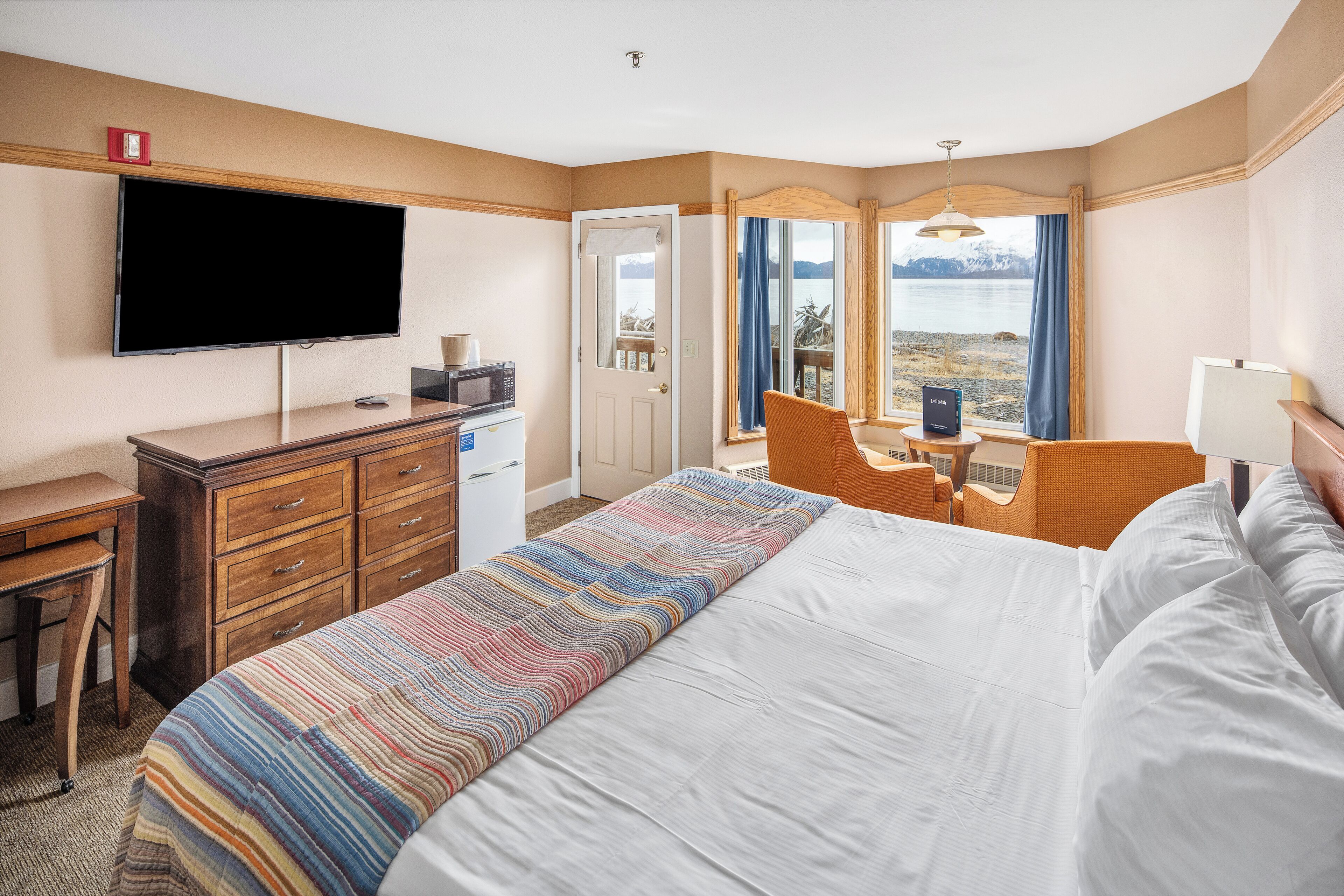 A hotel room with a large bed, a desk with a computer, a flat-screen TV, and a view of a lake.