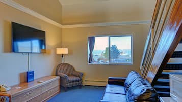 Habitación de hotel con una televisión de pantalla plana, un sillón estampado, un sofá de cuero, un escritorio con lámpara y una ventana con vistas a la ciudad.