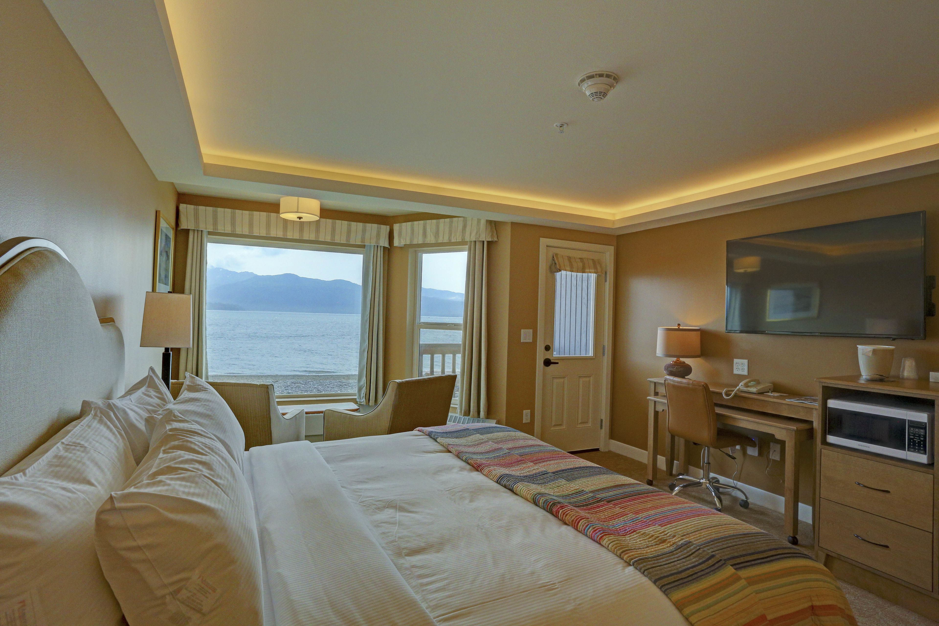 Habitación de hotel con una cama grande, un escritorio, una silla, televisión y vista al mar.