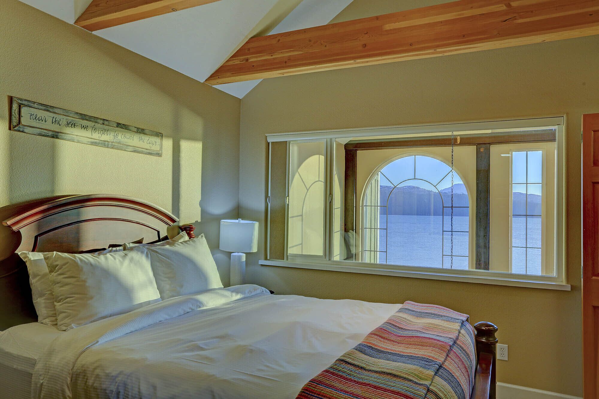 A bedroom with a bed, a window with a view of a lake, and a wooden ceiling.