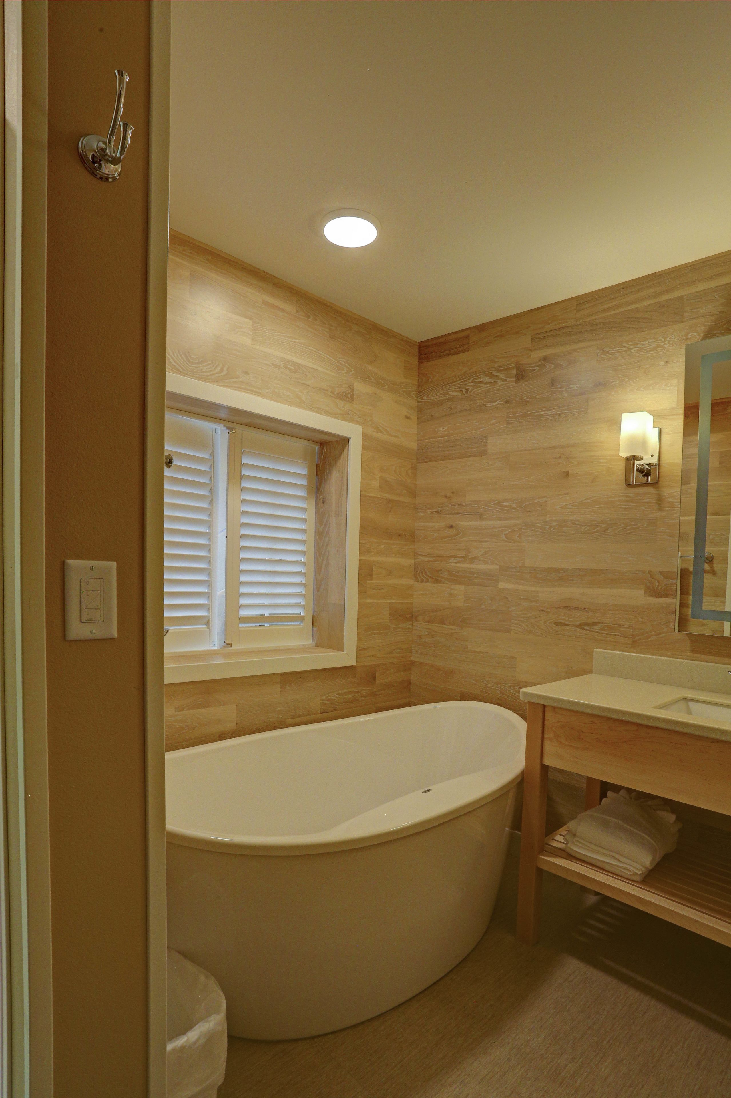 Une salle de bain avec une baignoire sur pieds, une fenêtre avec des stores, un meuble-lavabo avec un miroir et un luminaire fixé au mur.
