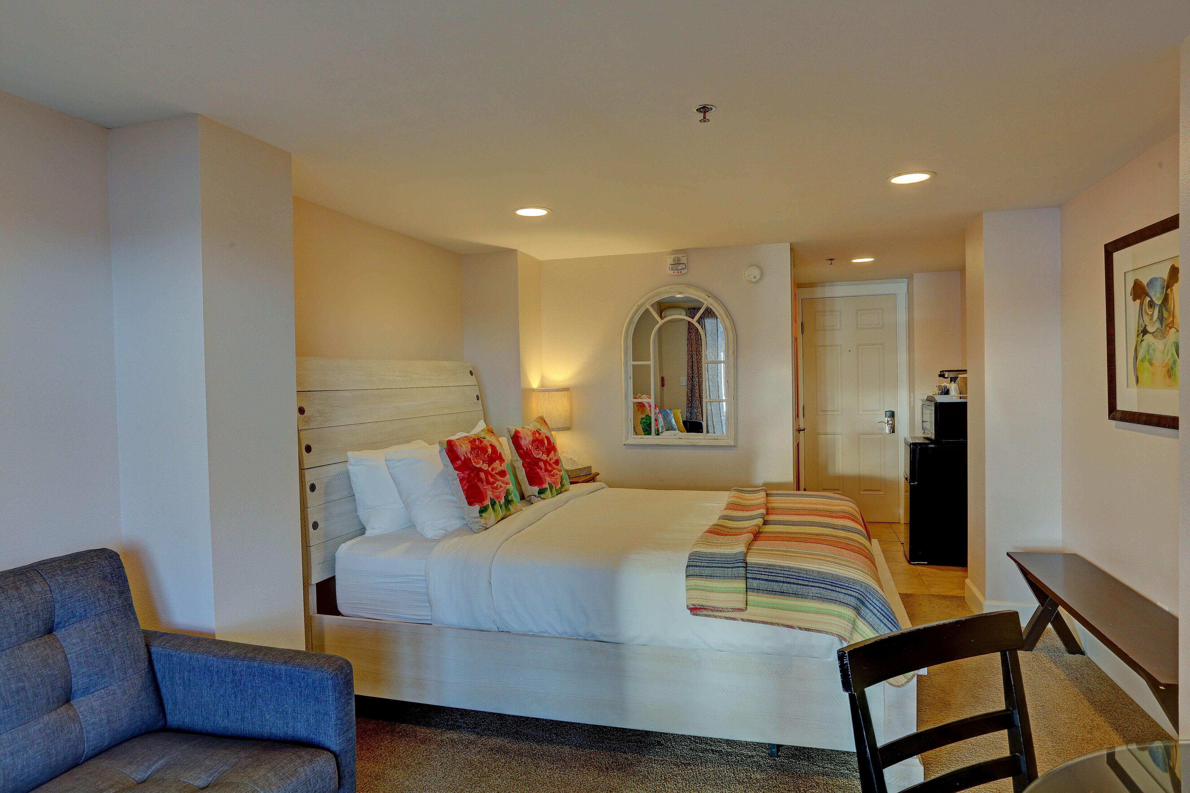 A hotel room with a bed, a chair, a desk, and a mirror.