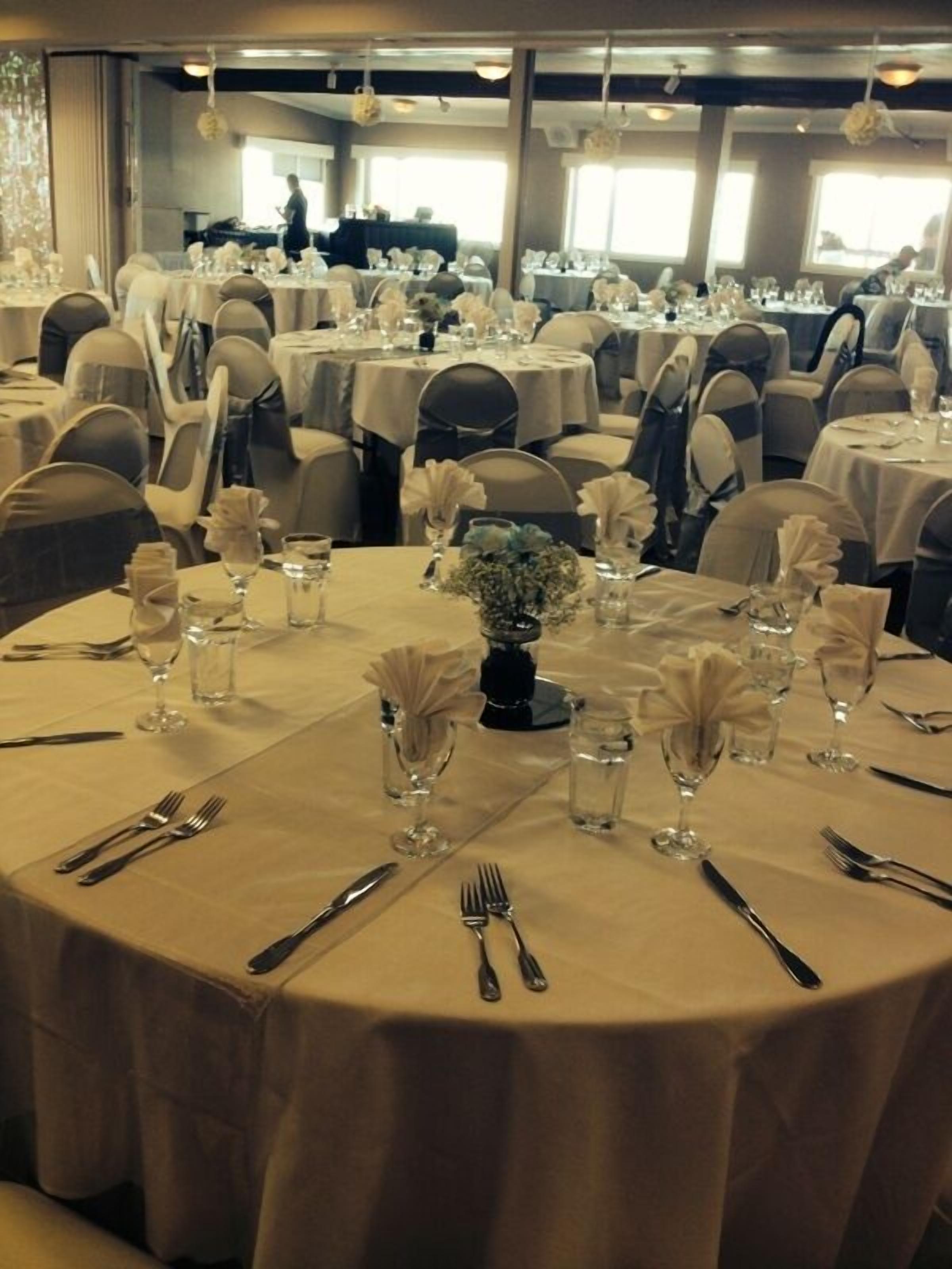 A banquet hall with round tables set for a formal event, featuring white tablecloths, glassware, and floral centerpieces.