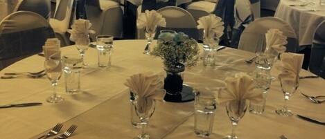 A banquet hall with round tables set for a formal event, featuring white tablecloths, glassware, and floral centerpieces.
