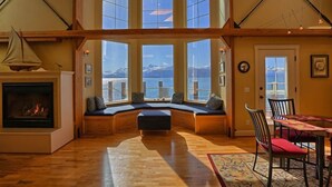 Ein gemütliches Zimmer mit Kamin, einer Fensterbank-Sitzgelegenheit mit Bergblick und einem Esstisch mit Stühlen.