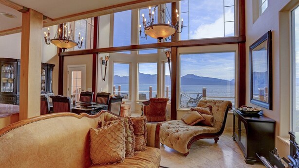 Ein geräumiges Zimmer mit großem Fenster, das Blick auf das Meer und die Berge bietet. Es gibt ein bequemes Sofa, einen Sessel und einen Esstisch mit Stühlen.