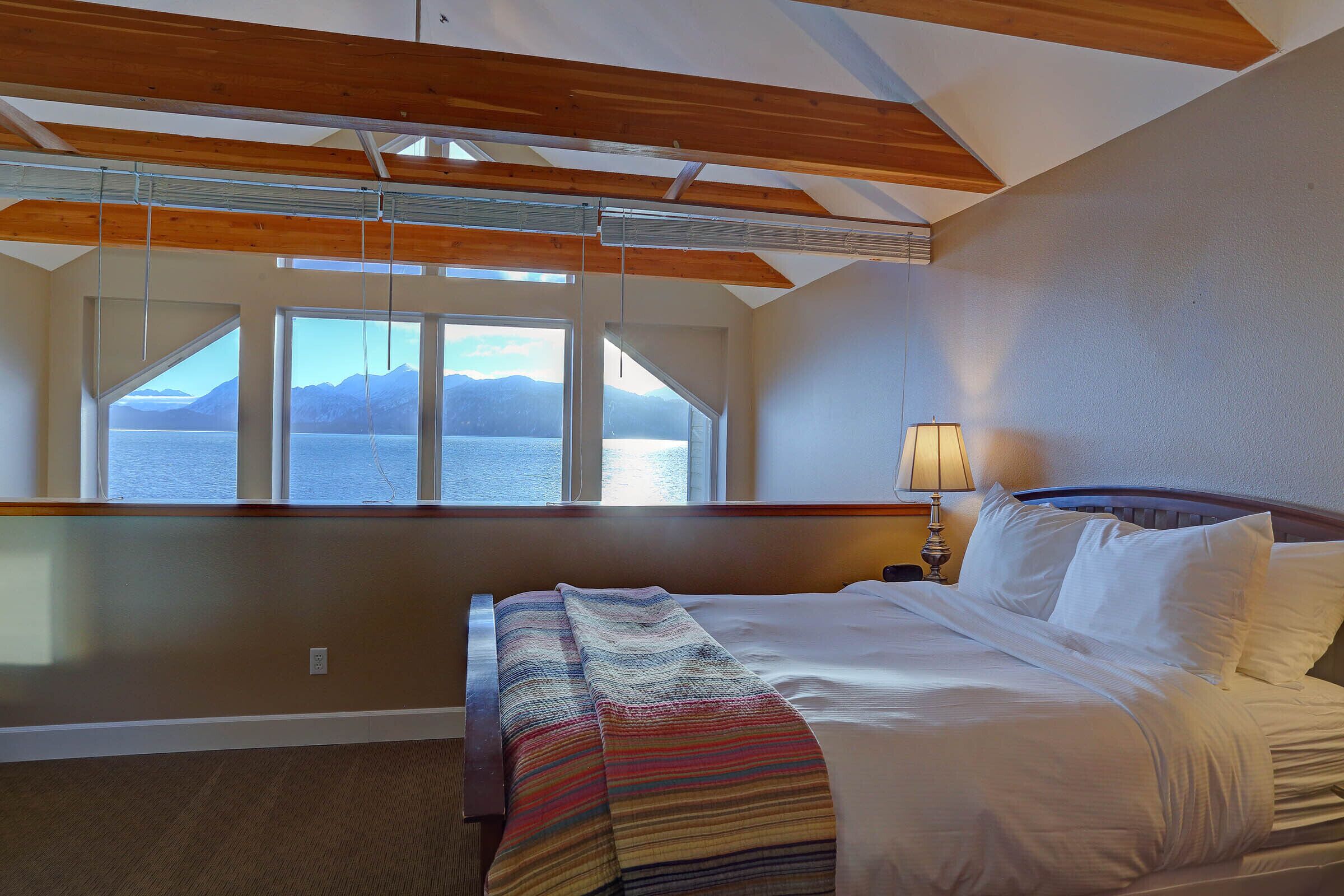 A bedroom with a bed, a window with a view of mountains, and a lamp on the nightstand.