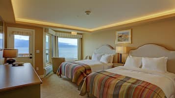 A hotel room with two beds, a desk, and a view of the sea.