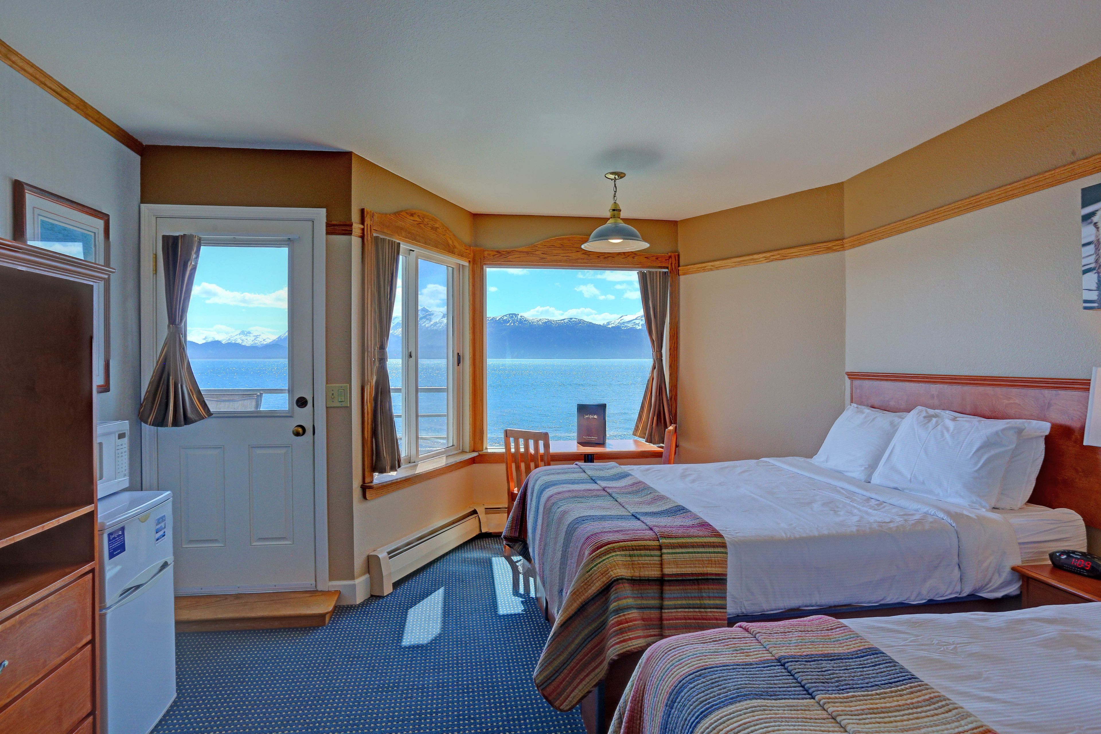 A hotel room with two beds, a desk, and a view of the sea.