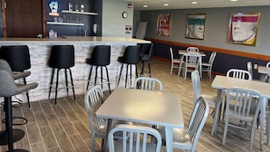 A restaurant interior with a bar area, multiple seating options including bar stools and tables, and wall decorations. - AmericInn by Wyndham Manitowoc (Manitowoc)