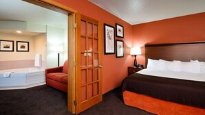 A hotel room with a bed, a red chair, a wooden door, a nightstand with a lamp, and a bathtub. - AmericInn by Wyndham Manitowoc (Manitowoc)