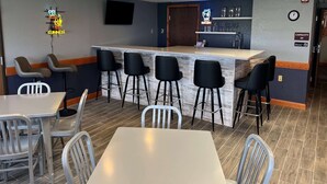 A bar area with a counter, stools, and a neon sign. There are tables and chairs around the bar. - AmericInn by Wyndham Manitowoc (Manitowoc)